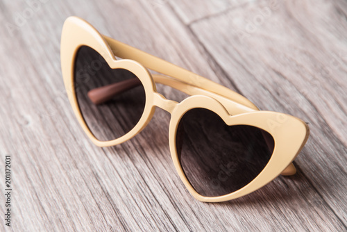 Stylish sunglasses in the form of hearts on a light wooden background