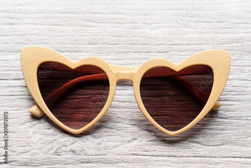 Beige sunglasses in the form of hearts on a light wooden background
