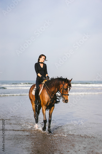front view of young female equestrian riding horse with ocean behind