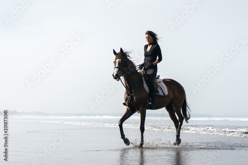 young woman riding horse on sandy beach with ocean behind