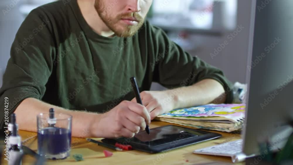 Young male designer using stylus and drawing tablet connected to computer to create illustrations Young male designer using stylus and drawing tablet connected to computer to create illustrations