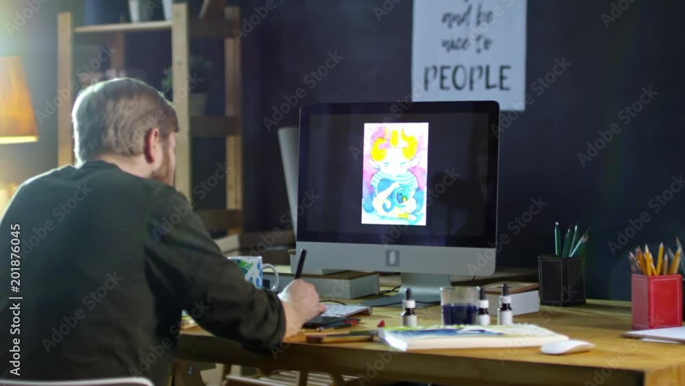 Rear view of male illustrator working with drawing tablet connected to computer to create picture of fantasy creature Rear view of male illustrator working with drawing tablet connected to computer to create picture of fantasy creature