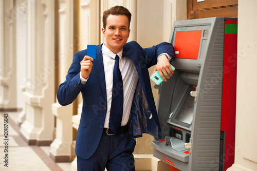 A young businessman stands near an ATM in a shopping center