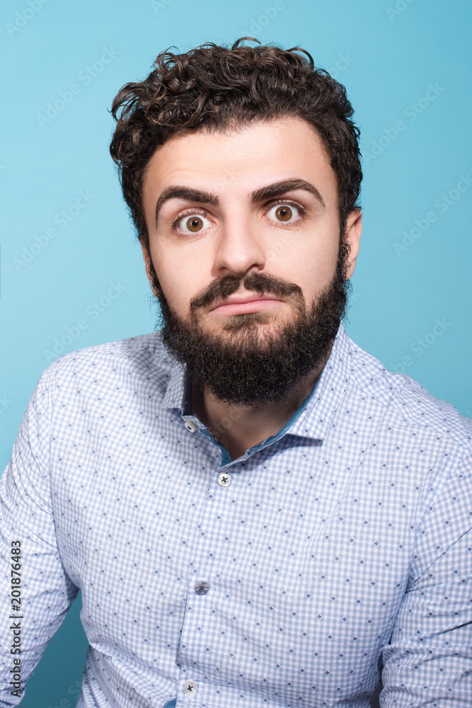 Shocking news. Studio portrait of a much surprised young man. The beard and blue shirt Shocking news. Studio portrait of a much surprised young man. The beard and blue shirt