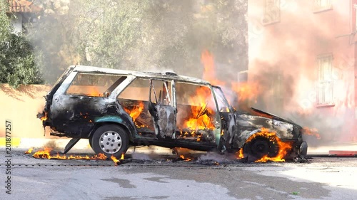 An abandoned import car on fire burns and later has something small explode while the horn blares. photo