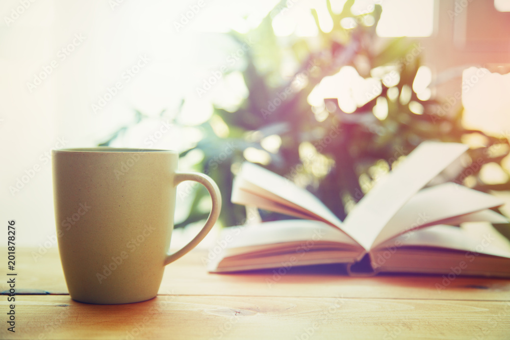 cup and open book on wooden table in front of the window cup and open book on wooden table in front of the window