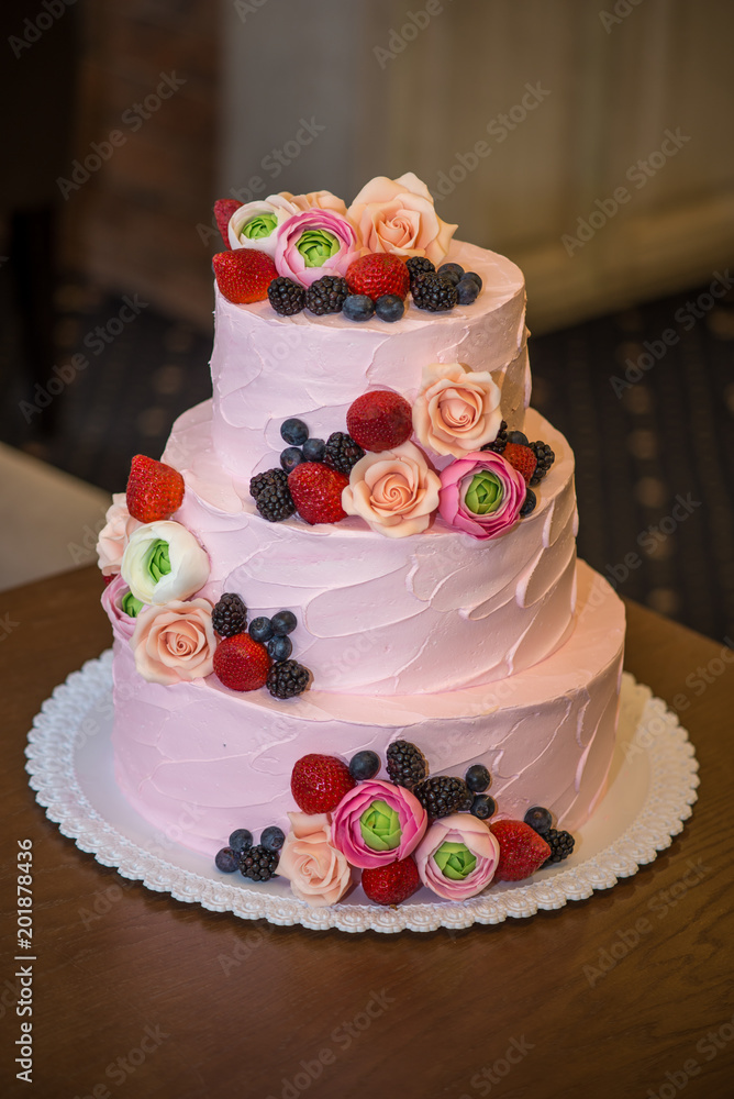 Three tiered pink wedding cake decorated with berries and flowers. Concept patisserie floristic from sugar mastic Three tiered pink wedding cake decorated with berries and flowers. Concept patisserie floristic from sugar mastic