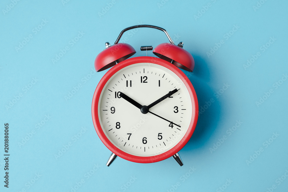 Red vintage alarm clock on light blue color background - obrazy, fototapety, plakaty 