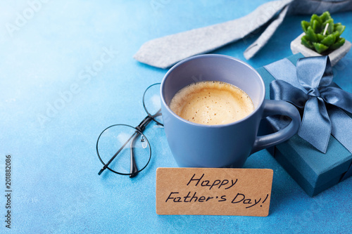 Happy Fathers Day card, cup of coffee, gift box and eyeglasses on blue table for breakfast.