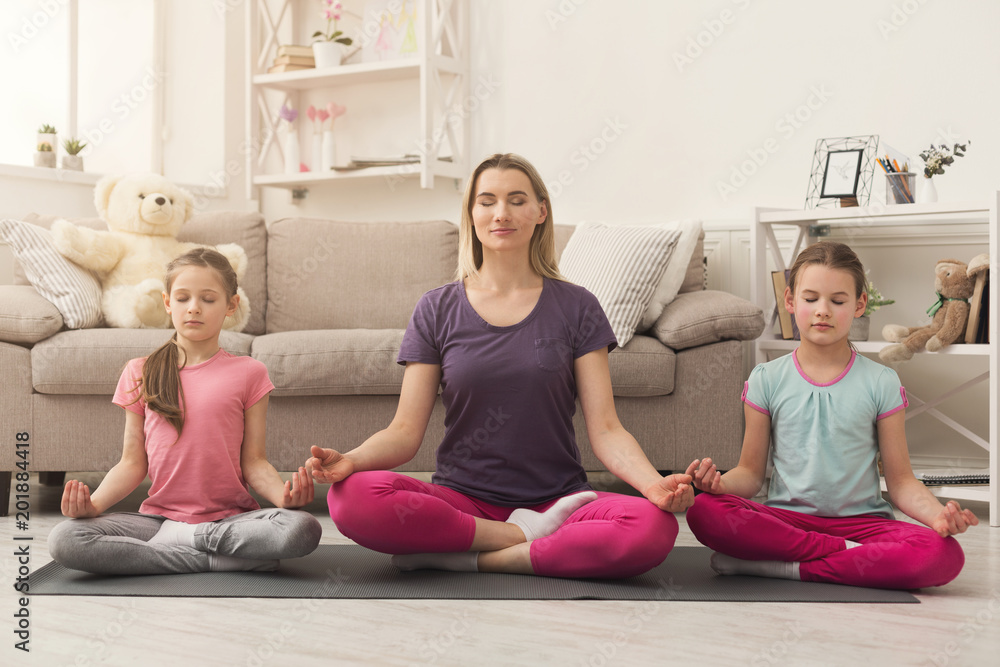 Young woman and daughters doing yoga exercise at home