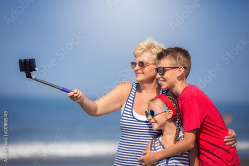Cute grandmother taking selfie with grandchildren on the beach