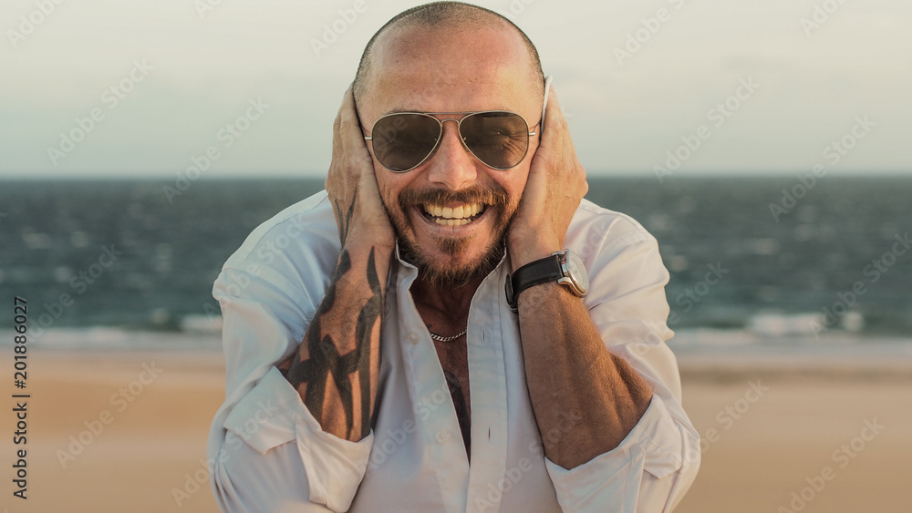 smiling and happy hipster MAN with tattoos and beard on a sandy and windy beach in spain