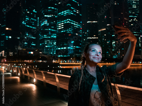 Photography Woman holding smartphone for self-portrait photo with view of modern skyscrapers