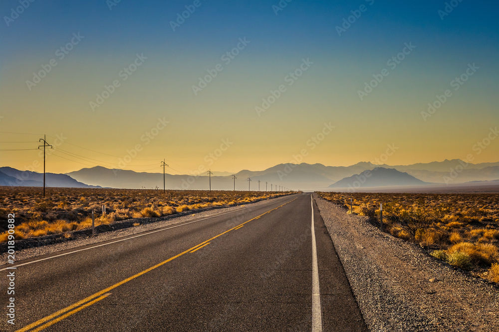 Scenic landscape in Death Valley National Park: a shiny road in the early morning with mountain range in the background, summer, California.