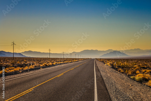 Scenic landscape in Death Valley National Park: a shiny road in the early morning with mountain range in the background, summer, California.