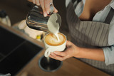 Closeup of barmen pouring milk to cappuccino cup
