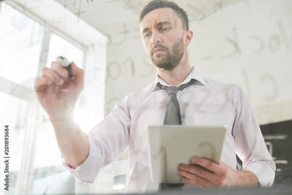Fototapeta premium Serious concentrated handsome bearded male programmer using tablet while analyzing web script on glassy board and editing data