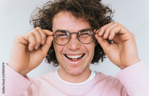 Cropped closeup portrait of handsome freckled positive male with curly hair and healthy toothy smile  corrects glasses posing for advertisement  isolated on white wall with copy space for your text.