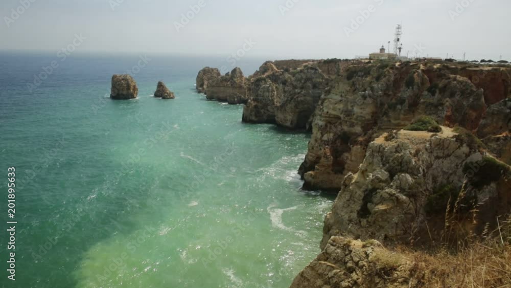 Spectacular Algarve coast with Ponta da Piedade lighthouse in the distance. Lagos, Algarve in Portugal. Tour tourism in Atlantic Ocean. Aerial view of rock formation and pillars of Lagos bay. Spectacular Algarve coast with Ponta da Piedade lighthouse in the distance. Lagos, Algarve in Portugal. Tour tourism in Atlantic Ocean. Aerial view of rock formation and pillars of Lagos bay.