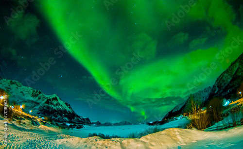 Northern lights shine bright and beautiful above sharp peaks and lakes of Lofoten mountains