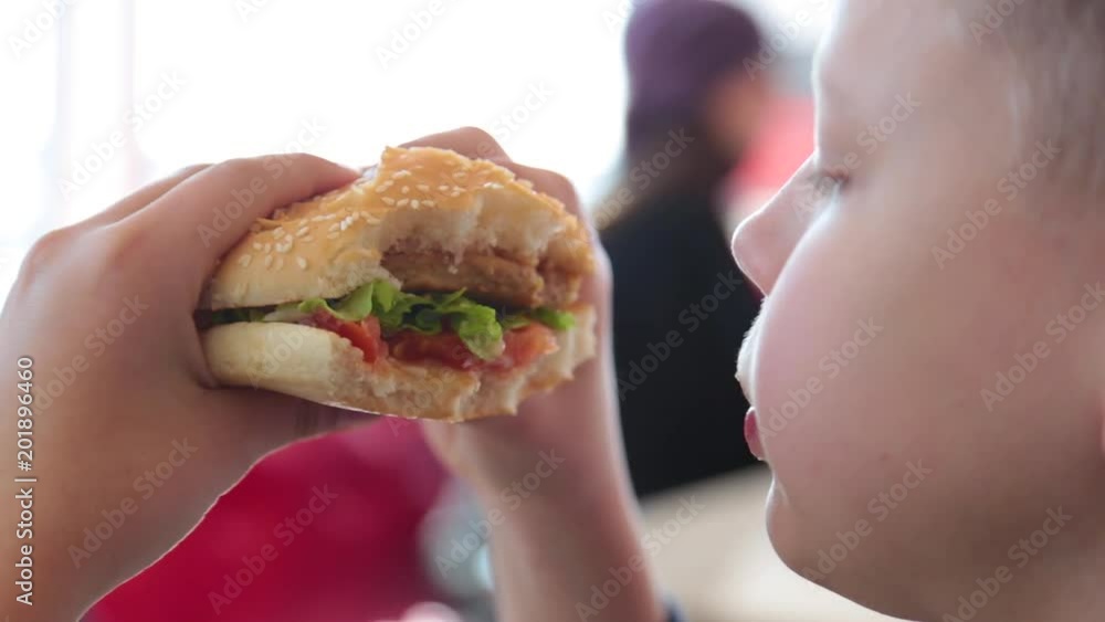Closeup view of white child eating juicy big hamburger at fast food restaurant. Real time full hd video footage. Closeup view of white child eating juicy big hamburger at fast food restaurant. Real time full hd video footage.