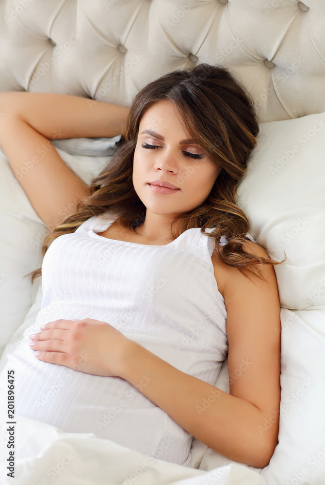 A beautiful pregnant woman sleeps in a white bed. Conception of pregnancy, motherhood. A beautiful pregnant woman sleeps in a white bed. Conception of pregnancy, motherhood.