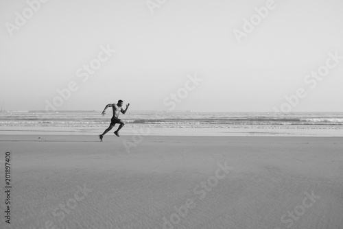 Black man running by the sea on the beach. Powerful runner sprinting and training on summer.