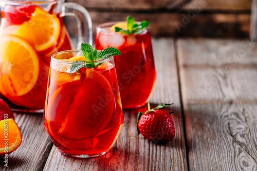 Homemade red wine sangria with orange, apple, strawberry and ice in glass and pitcher on wooden background.