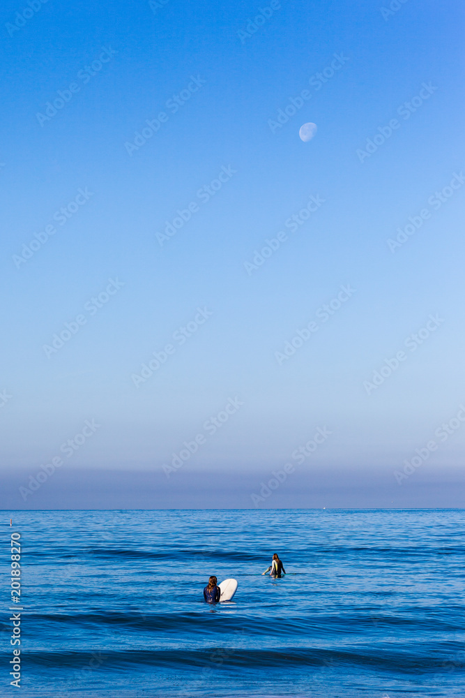 Surfers on the moonlight beach with moon hanging above the sky