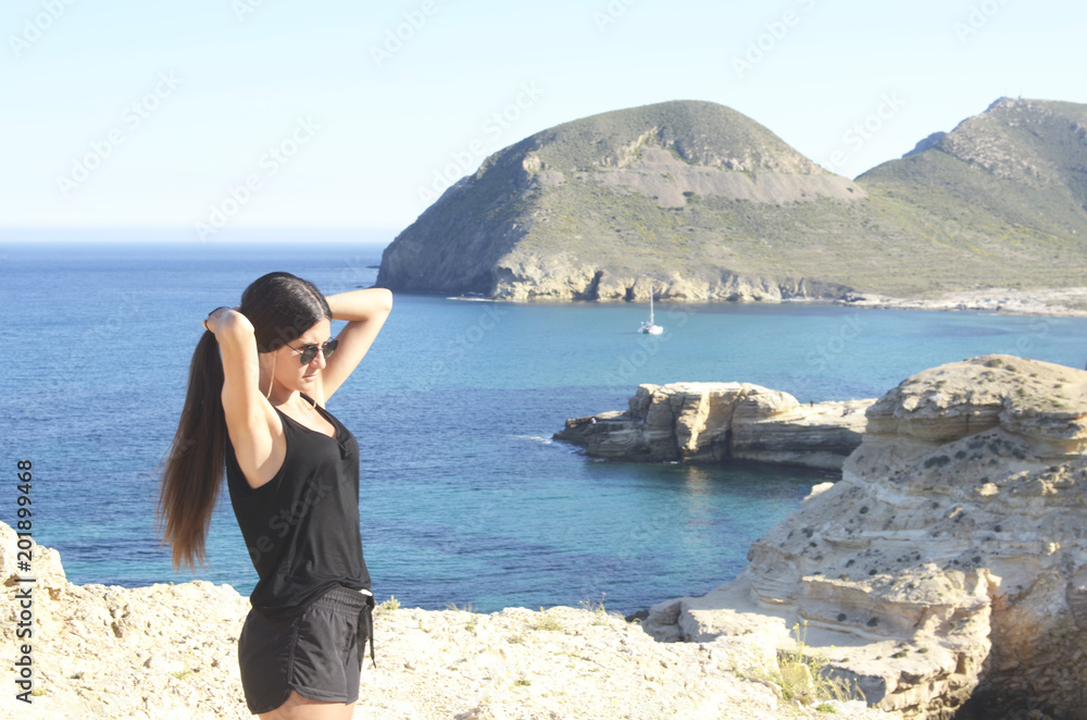 Young woman standing on the edge makes a ponytail. she is on the cliffs on the mediterranean rocky coast Young woman standing on the edge makes a ponytail. she is on the cliffs on the mediterranean rocky coast
