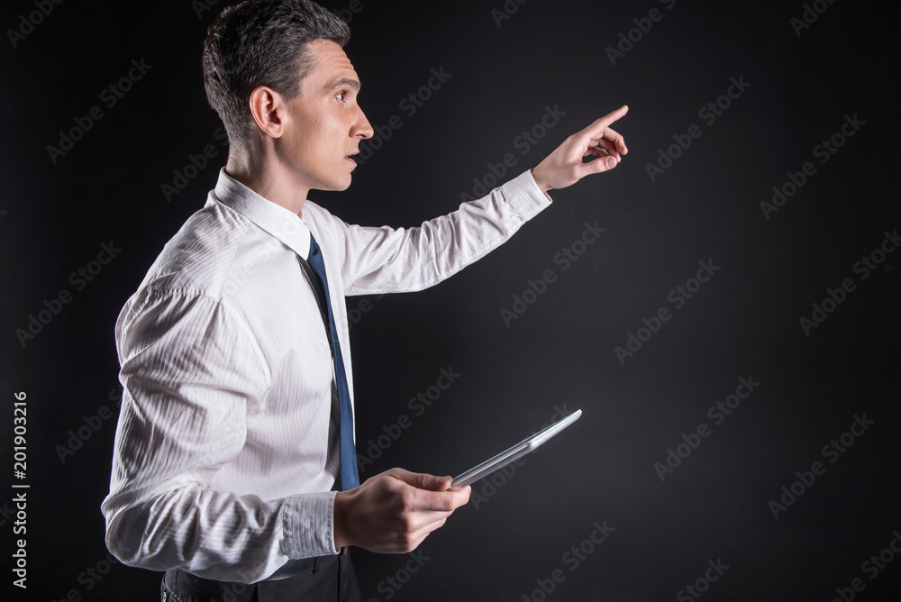 Working process. Pleasant nice adult man holding a tablet and pointing at the screen while focusing on working process Working process. Pleasant nice adult man holding a tablet and pointing at the screen while focusing on working process