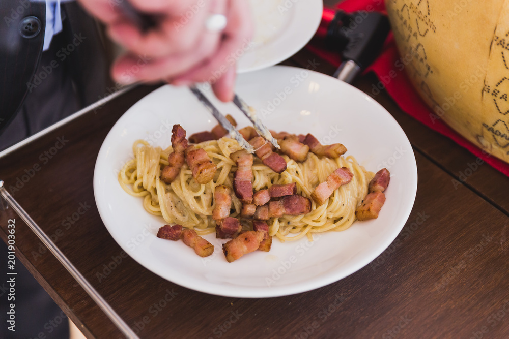 Fototapeta premium Spaghetti Carbonara made in cheese wheel topping with fried bacon on white plate.