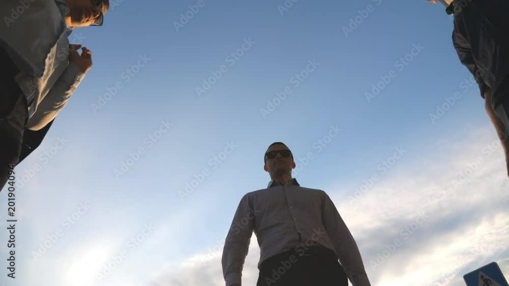 Low angle view of three business men standing outdoor near office and talking. Businessmen meet and speaking outside in the city with blue sky at background. Communication of happy colleagues. Closeup Low angle view of three business men standing outdoor near office and talking. Businessmen meet and speaking outside in the city with blue sky at background. Communication of happy colleagues. Closeup