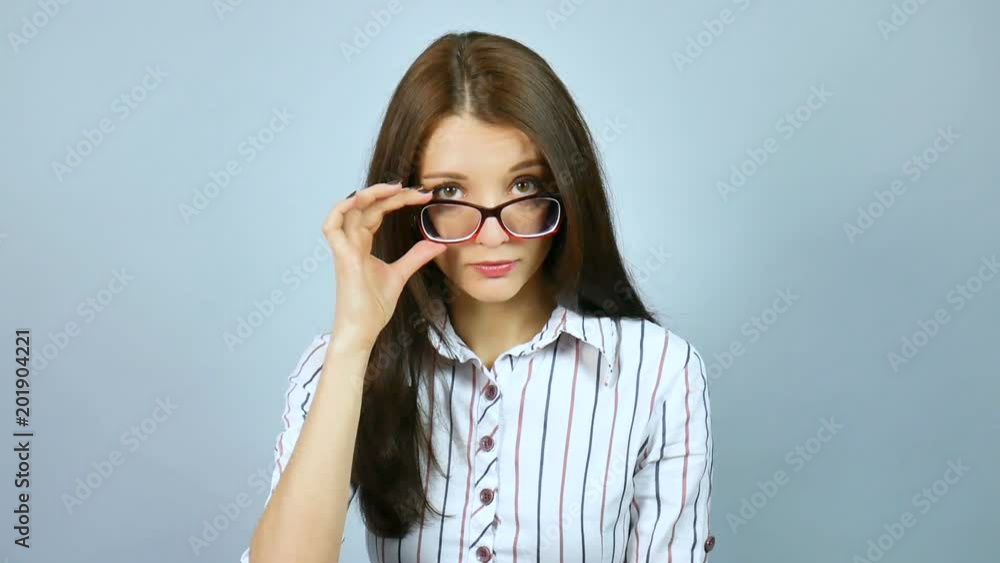 Young Strict Exacting Female Teacher Wearing Optical Eyeglasses Looking at the Camera in Studio on Grey Background. Young Strict Exacting Female Teacher Wearing Optical Eyeglasses Looking at the Camera in Studio on Grey Background.