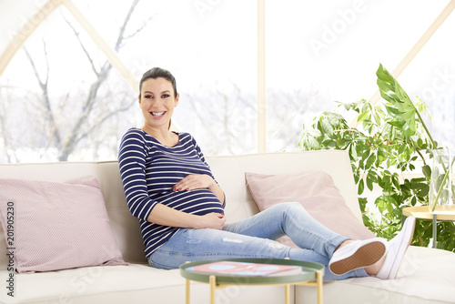 Woman enjoys her pregnancy. Full length shot of beautiful pregnant woman sitting on sofa while relaxing at home.