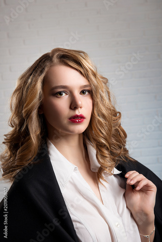 A blonde girl with makeup and hairdo in stylish clothes against a white brick wall background.