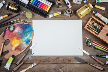 Set of artist accessories collection. Canvas, tube of oil paint, art brushes, palette knife lying on the wood table. Artist workshop background.