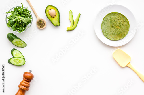 Make spinach pancakes. White background with spinach leaves, avocado, cucumber, spatula and spices top view copy space