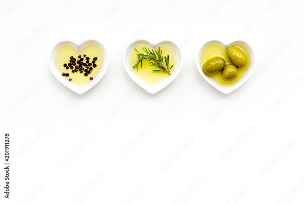 Olive oil as famous product of mediterranean cuisine. Heart shaped bowls  with olive oil with green olives, rosemary and black pepper inside on white  background top view copy space Stock Photo