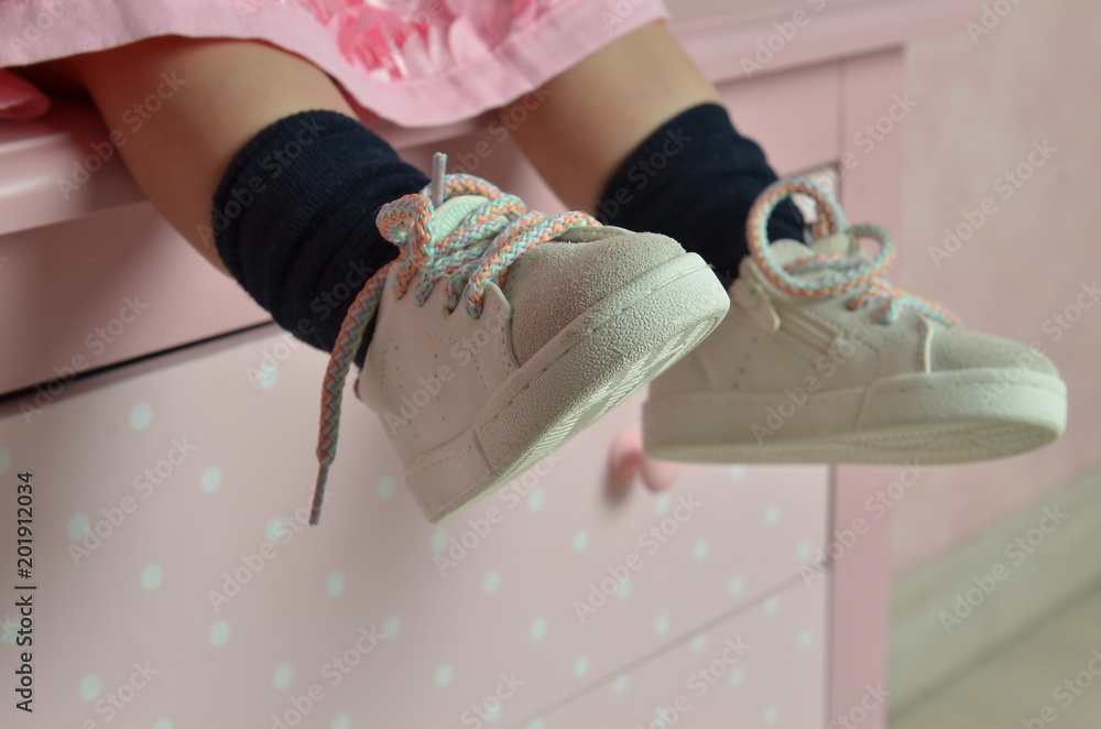 Legs of a little girl sitting on a dresser. close-up shot of the baby's ...
