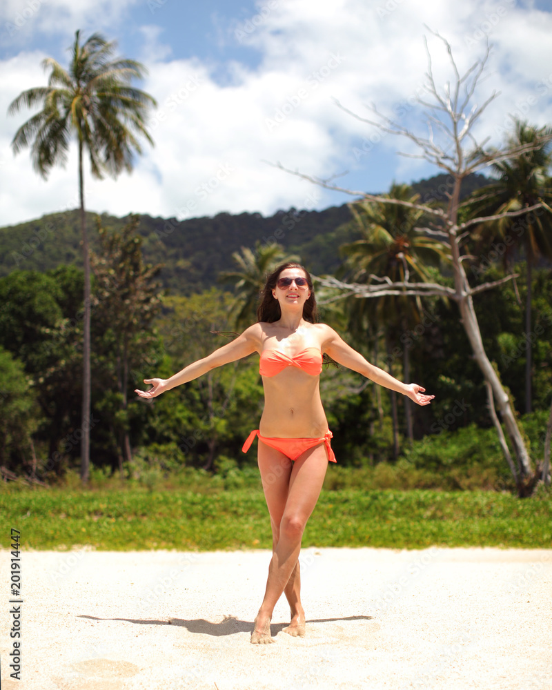 Young woman in red bikini standing on the fine sand beach, arms spread, with palms in background. Klong Jak Beach, Koh Lanta, Thailand Young woman in red bikini standing on the fine sand beach, arms spread, with palms in background. Klong Jak Beach, Koh Lanta, Thailand