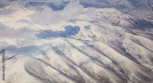 Snowy mountains background and white clouds above them. Aerial photo from plane window.