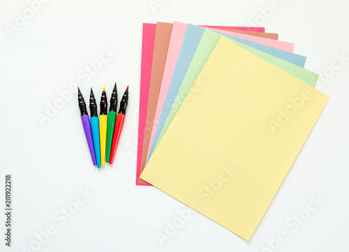 brightly colored paint pens with fanned out multicolored construction paper isolated on white