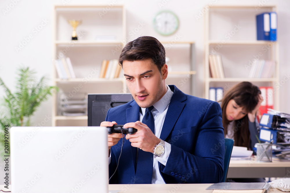 Man playing games in office while colleague is busy Man playing games in office while colleague is busy