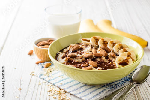 Oatmeal porridge with banana, almonds and chocolate syrup on white wooden background © nesavinov
