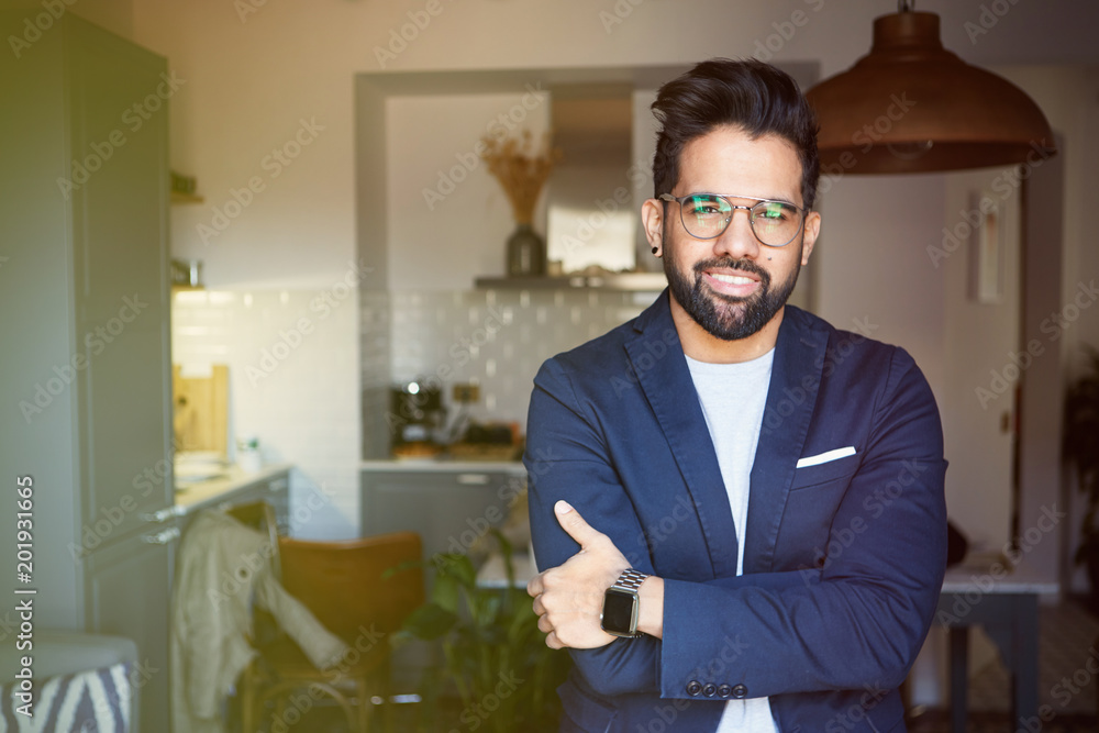 Smiling bearded man taking poising at home. Young handsome man looking at camera while standing in center of living room.Blurred background Smiling bearded man taking poising at home. Young handsome man looking at camera while standing in center of living room.Blurred background