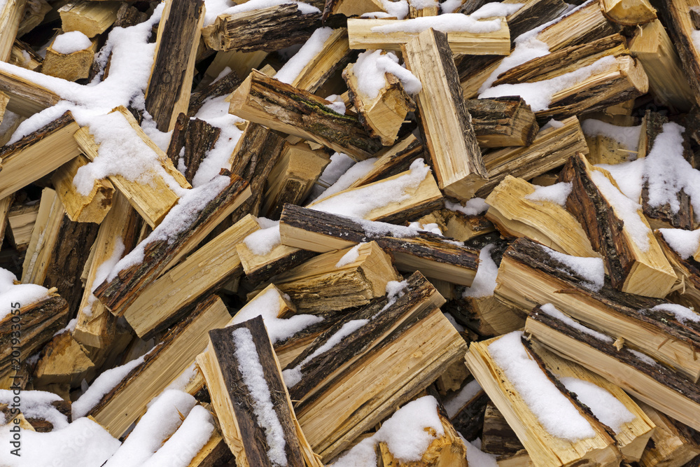 background - a messy heap of chopped logs lightly covered with fallen and melting snow background - a messy heap of chopped logs lightly covered with fallen and melting snow