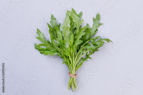 Bunch of arugula with brown twine. Fresh organic rucola on textured background. Tasty and nutritious plant.