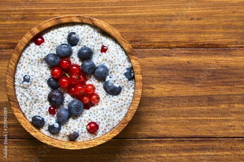 Chia (lat. Salvia hispanica) seed pudding with blueberries and redcurrants in wooden bowl, photographed overhead on wood with natural light (Selective Focus, Focus on the top of the pudding)