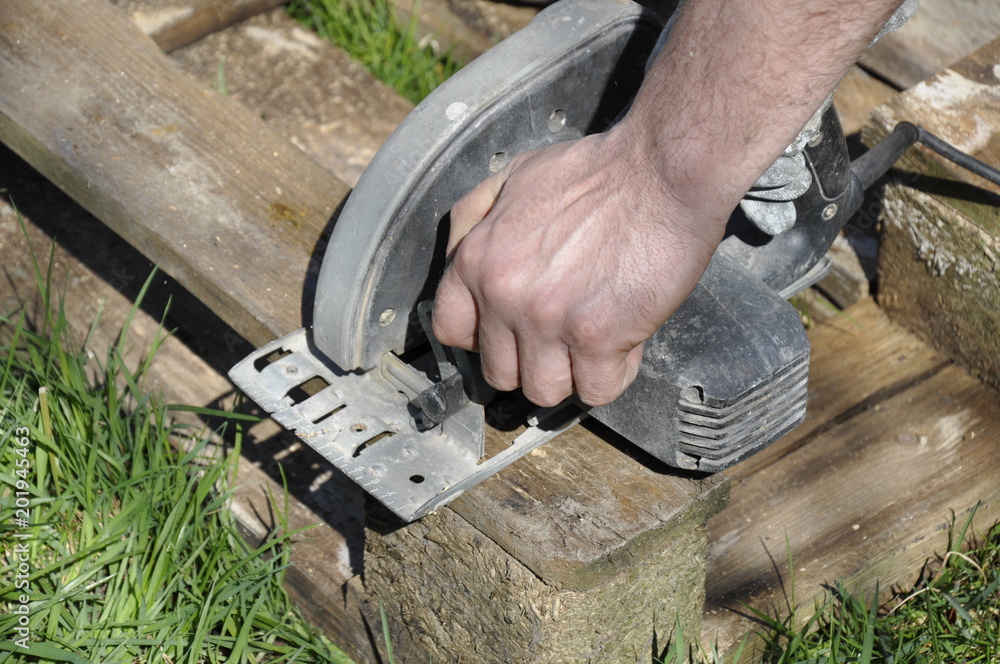 close-up of the hand of a man holding an electric saw and cutting old boards close-up of the hand of a man holding an electric saw and cutting old boards